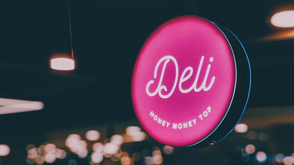 Deli logo sign on a pink neon light in a dark background