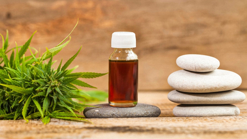 CBD oil in the middle of the image with hemp leaves on the left and three white stones on top of each other on the right