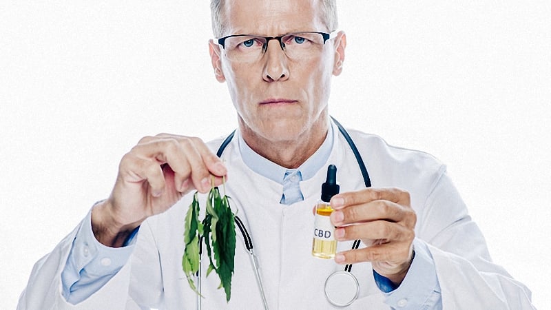 A doctor looking at the camera holding cbd oil bottle and hemp leaves on his hands