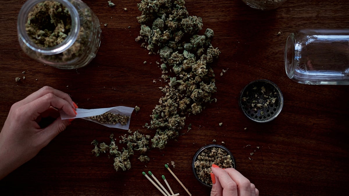 Person rolling a marijuana paper joint on a wooden table with cannabis lying around