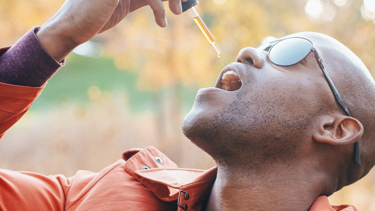 Person wearing sunglasses taking cbd oil from a dropper