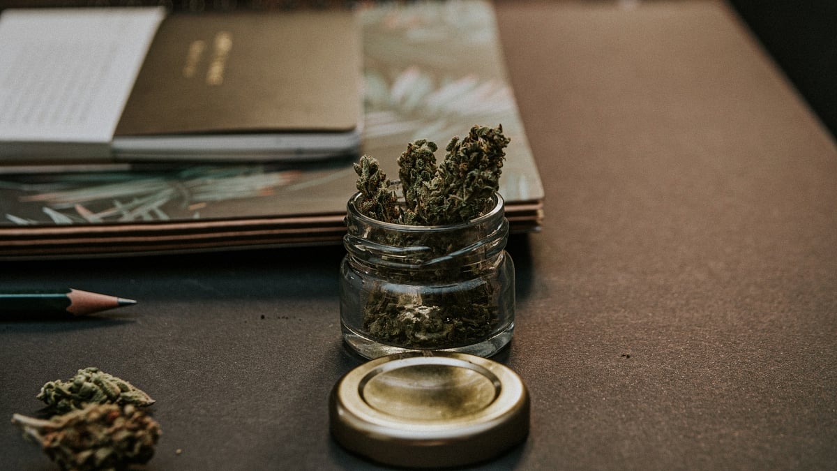 A jar containing cannabis buds on a wooden office desk background
