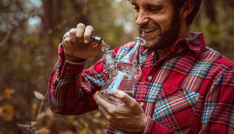 Man wearing a red button shirt smoking marijiuana from a glass bong