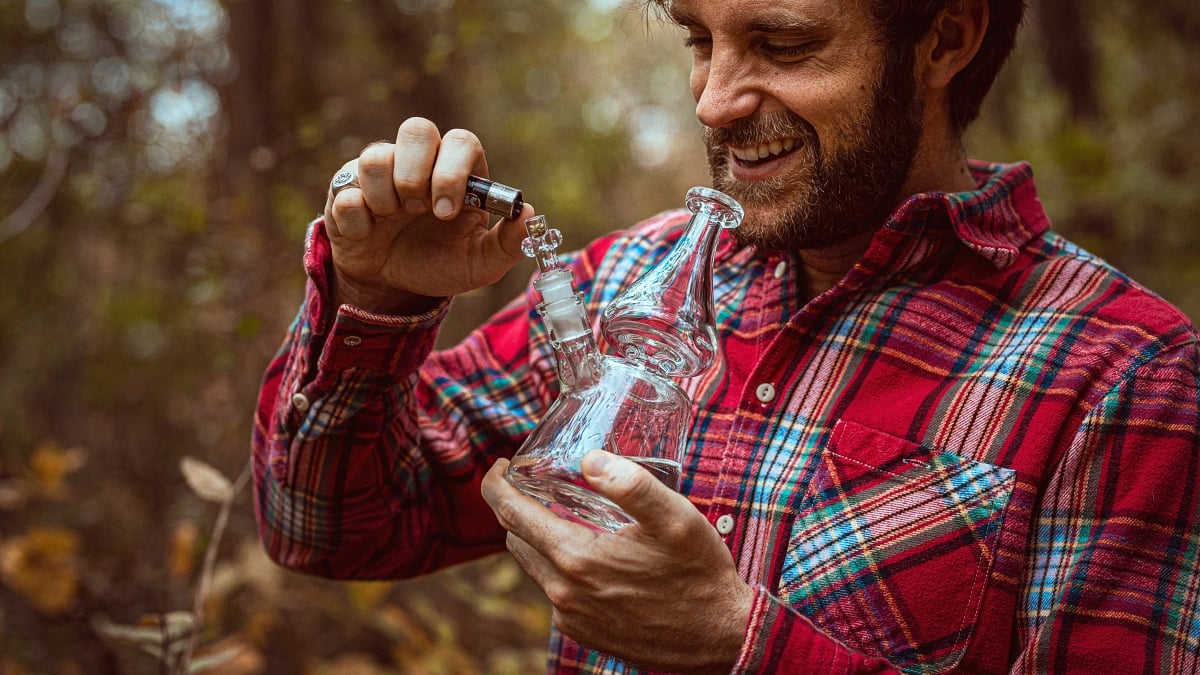 Man wearing a red button shirt smoking marijiuana from a glass bong