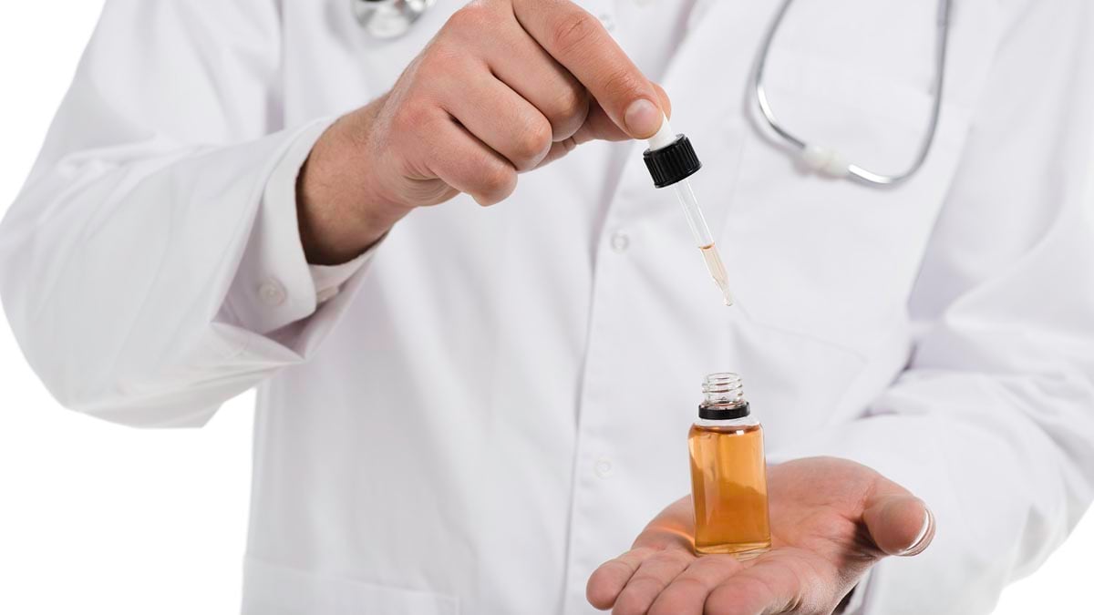 cropped view of male doctor opening up bottle with cbd oil and dropper isolated on white