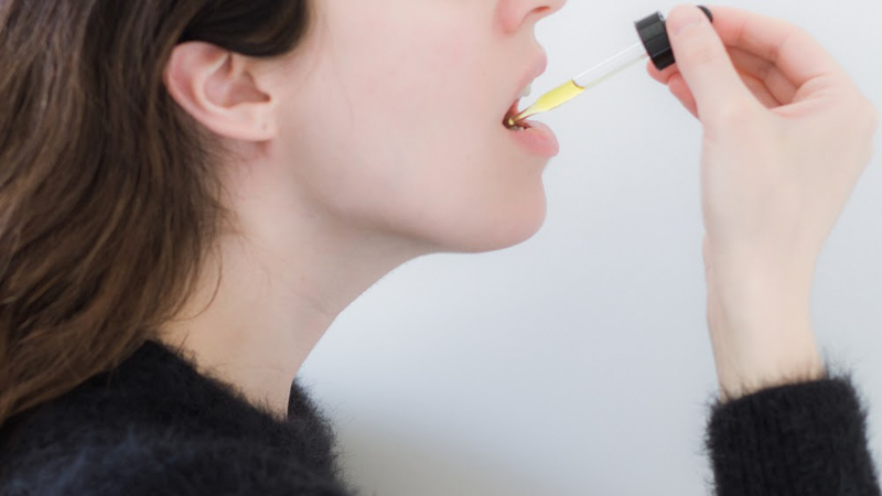 A woman taking CBD oil from a glass dropper in white background