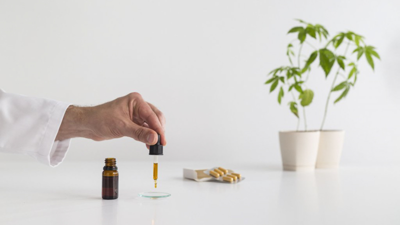 A doctor's hand pouring CBD oil out of a dropper on to a white tabke