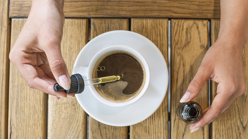 mixing cbd oil into a cup of coffee on a wooden table