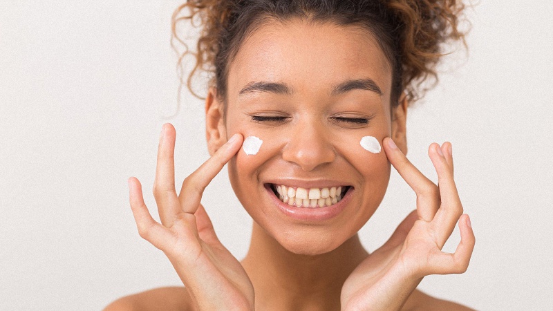 Woman happily applying skincare cream on her face