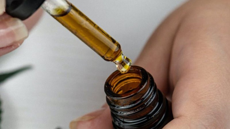 Hand Holding CBD Oil Dropper Near its Bottle