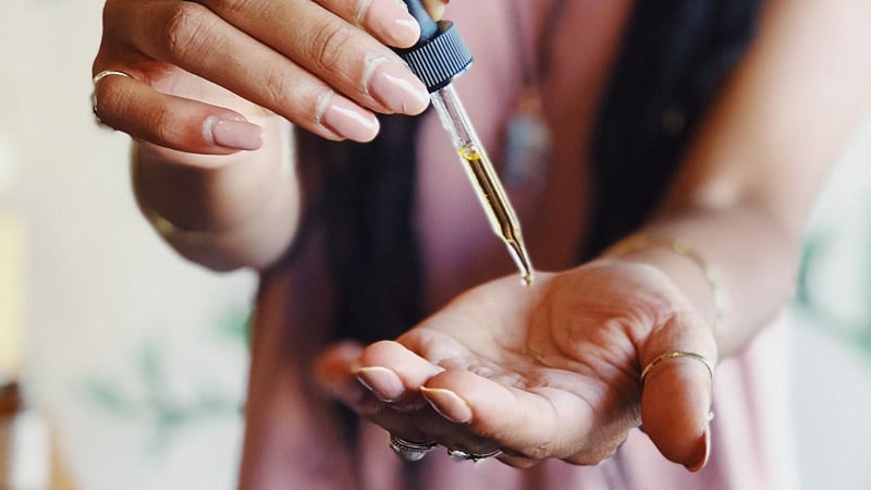 woman taking CBD oil on hand using a dropper